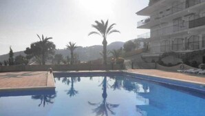 Ein Pool mit klarem Wasser, das Palmen und ein mehrstöckiges Gebäude im Hintergrund spiegelt.