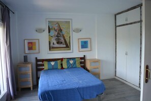 Ein Schlafzimmer mit einem Bett, Nachttischen aus Holz, einem Kleiderschrank und zwei gerahmten Kunstwerken an der Wand.