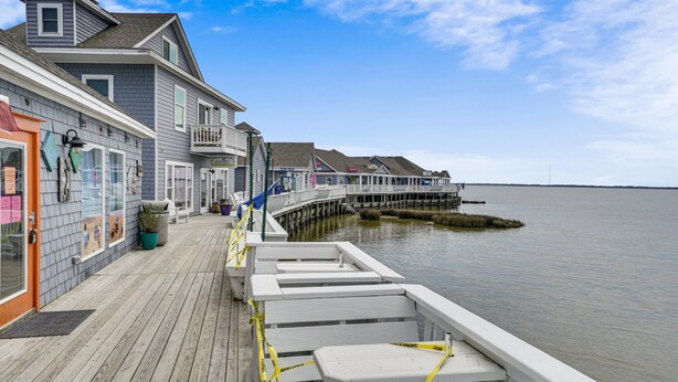 A waterfront property with a wooden deck, a pier extending into the water, and a building with a balcony. - Adorable Beach house in Duck with Hot Tub, Pet friendly.  Roof top deck! (Duck)