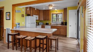 A kitchen with wooden cabinets, a white refrigerator, a microwave, and a bar stool area. - Adorable Beach house in Duck with Hot Tub, Pet friendly.  Roof top deck! (Duck)