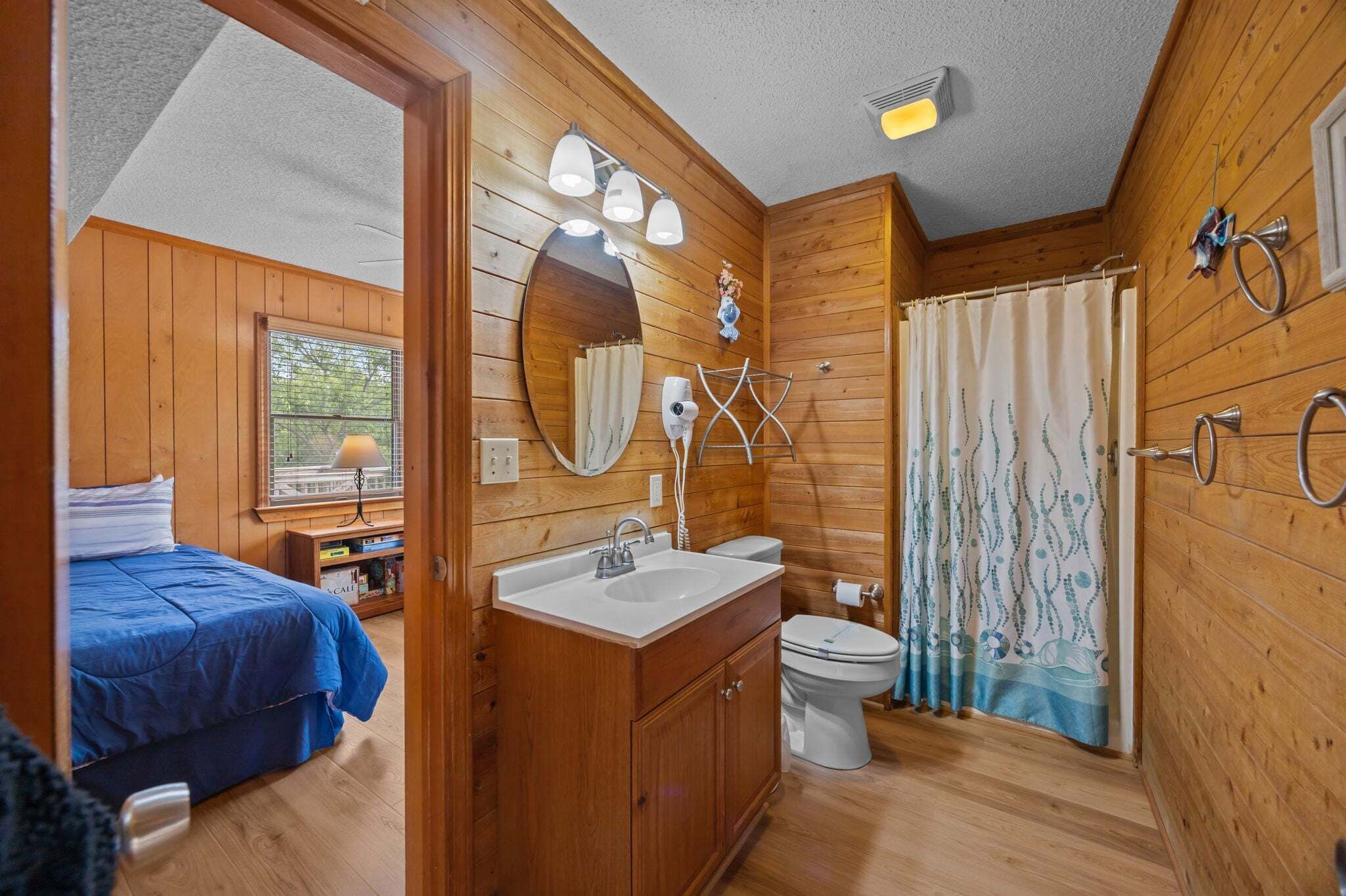 A wooden cabin interior with a bed, a bathroom with a sink, toilet, and shower curtain.