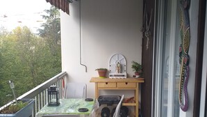 A balcony with a table, chairs, a small desk, and potted plants. - The secret of good taste. (Vaulx-en-Velin)