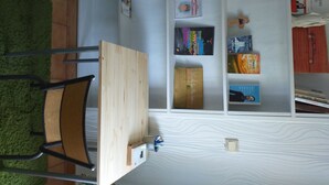 A room with a wooden desk, a chair, and a white shelving unit with books and decorative items. - The secret of good taste. (Vaulx-en-Velin)