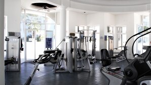 A gym with various exercise machines, large windows, and a ceiling fan.