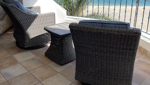 A balcony with wicker furniture, a view of the ocean, and palm trees.