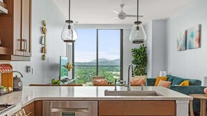 Une cuisine moderne dotée d’un grand îlot central, d’un coin repas avec un canapé vert et offrant une vue sur l’extérieur.