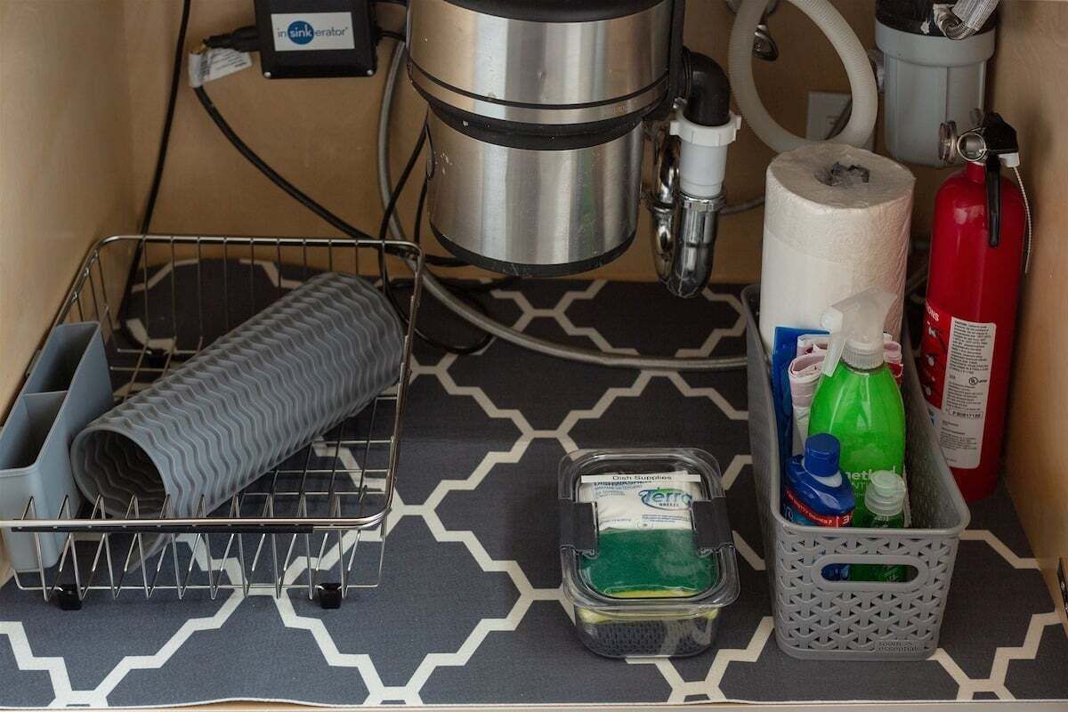 Een kitchenette met een koffiezetapparaat, een brandblusser, een rol keukenpapier, een draadmanden en een plastic bak met schoonmaakmiddelen.