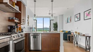 Une cuisine moderne dotée d’un îlot central, d’appareils électroménagers en acier inoxydable, de luminaires suspendus et offrant une vue par les fenêtres.