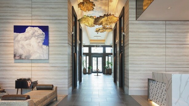 Un hall d’hôtel moderne avec un long couloir, un comptoir d’accueil et un espace détente comprenant un canapé et des fauteuils.