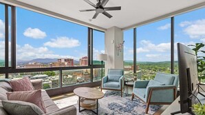 Ein modernes Wohnzimmer mit großem Fenster, Deckenventilator, Flachbildfernseher und Sofa.