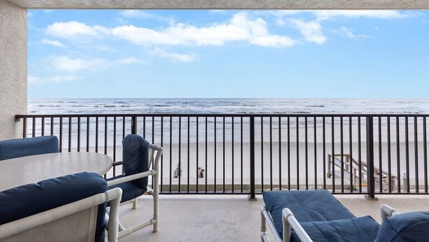 Un balcon avec vue sur la plage, une table et deux chaises.