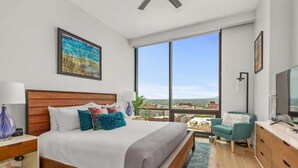 A hotel room with a large bed, a TV, a desk, and a view of the city.