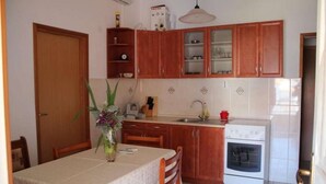 A kitchen with wooden cabinets, a white oven, and a dining table set with chairs. - Apartment in Pirovac with Terrace, Air condition, WIFI, Washing machine (4793-1) (Pirovac)