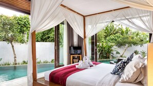 Una camera da letto con un letto a baldacchino, una piscina e rigogliosa vegetazione visibile attraverso ampie finestre.