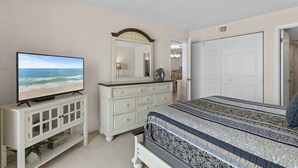 Un dormitorio con cama, cómoda, televisor y puerta.