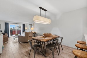 Un comedor con una mesa de madera, sillas de metal, una lámpara colgante y vista al exterior.