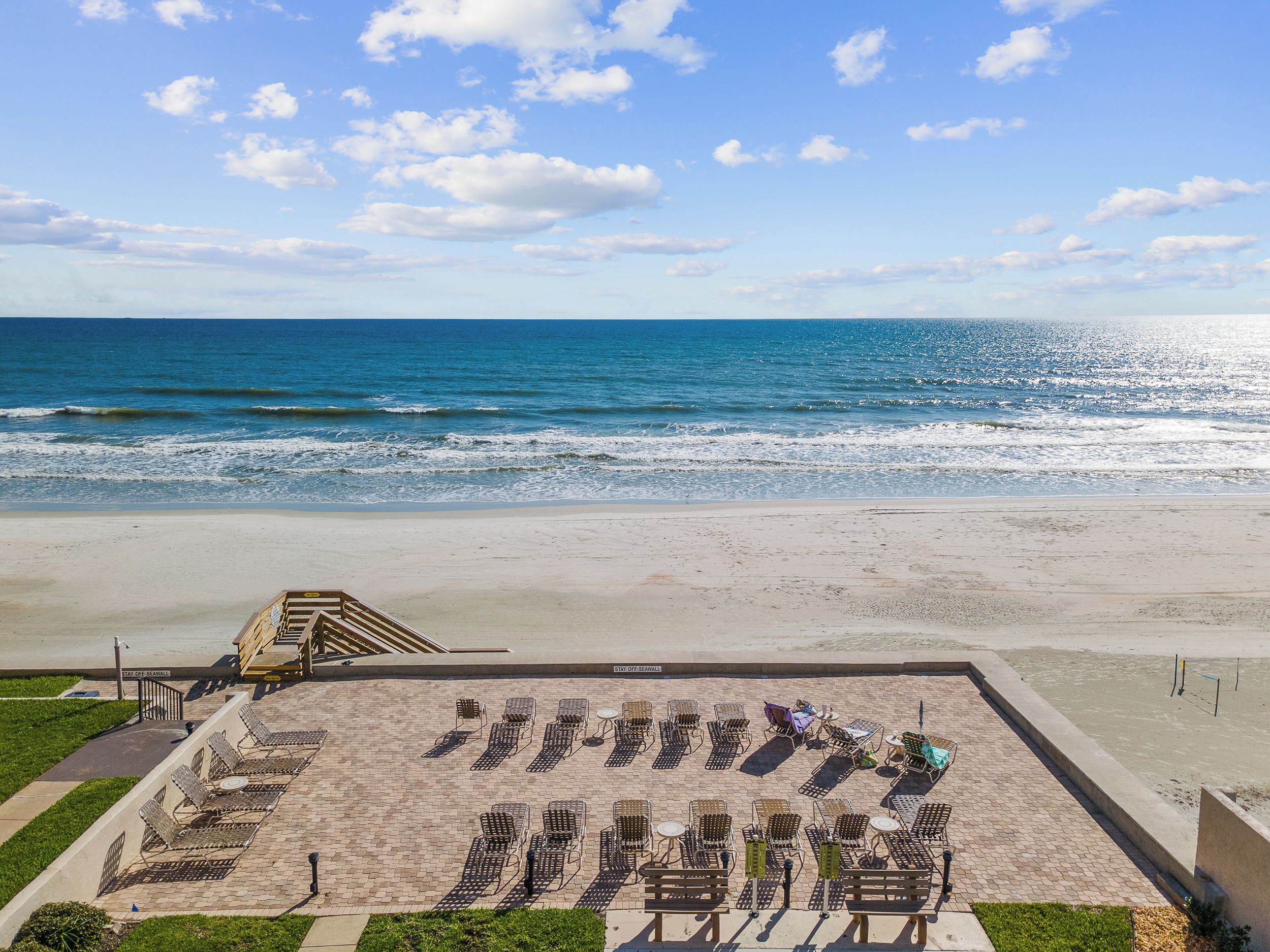 Une vue sur la plage avec une zone aménagée, comprenant des chaises longues et un escalier menant à une plateforme surélevée.