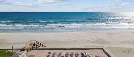 Une vue sur la plage avec une zone aménagée, comprenant des chaises longues et un escalier menant à une plateforme surélevée.