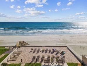 A beachside view with a paved area featuring sun loungers and a staircase leading to a higher platform. - 206 - Ocean View 2 bedroom (New Smyrna Beach)