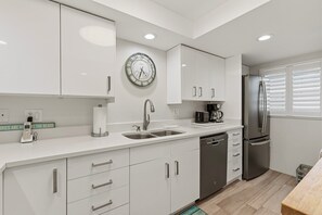 Una cocina moderna con armarios blancos, un refrigerador de acero inoxidable, una cafetera y un reloj en la pared.