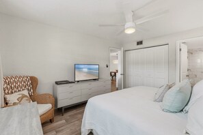 Ein Schlafzimmer mit einem Bett, einem Fernseher, einer Kommode, einem Sessel und einer Tür.