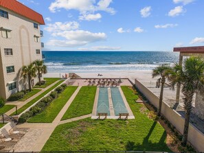 A beachfront property with a tennis court, lounge chairs, and a view of the ocean. - 206 - Ocean View 2 bedroom (New Smyrna Beach)