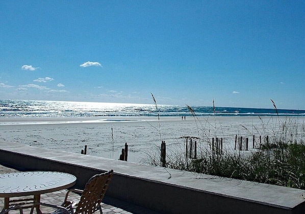 A beach view with a table and chairs, a concrete wall, and a wooden fence.