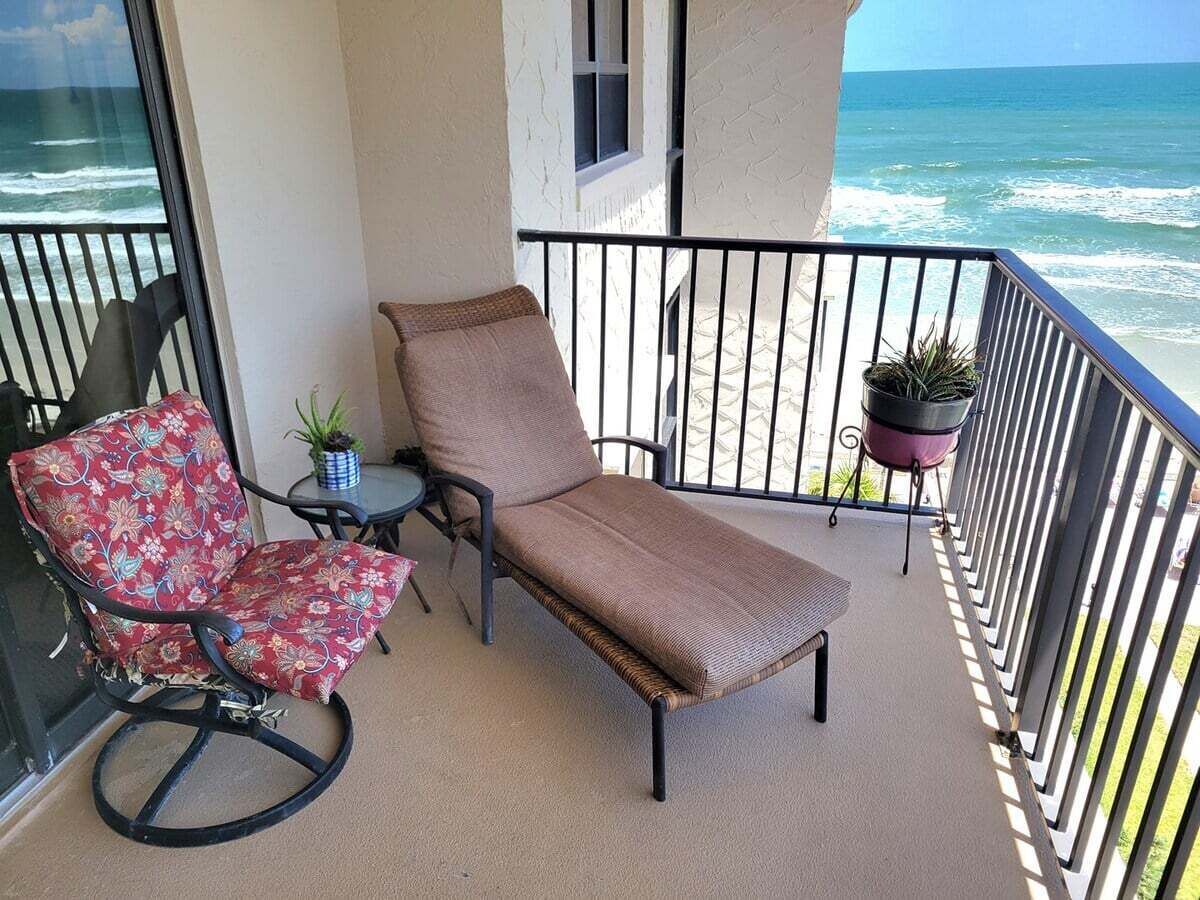 Een balkon met een lounge stoel, een schommelstoel, een klein tafeltje en een plant in pot.