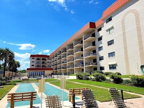 A multi-story hotel with balconies, a swimming pool, and a well-maintained lawn.
