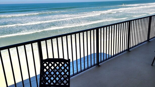 Ein Balkon mit Blick auf das Meer, ein schwarzer Stuhl und ein Metallgeländer.
