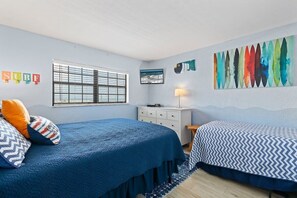 A bedroom with two beds, a window, a dresser, and wall art.