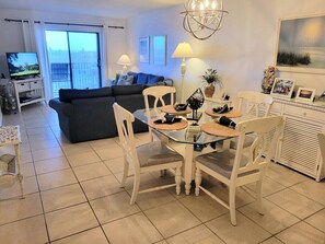 Un'area pranzo con un tavolo in vetro, sedie bianche e vista sul soggiorno.