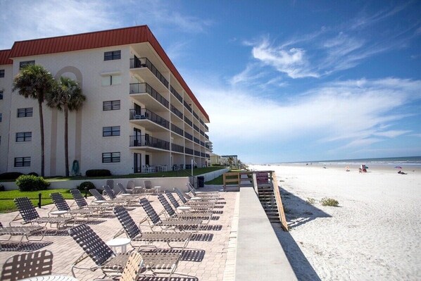 A hotel with multiple balconies, a beachside location, and sun loungers.