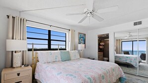 Une chambre avec un grand lit, une table de chevet, un ventilateur de plafond, une fenêtre avec des rideaux et une vue sur l’extérieur.
