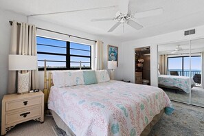 Una camera da letto con un letto grande, un comodino, una ventola a soffitto, una finestra con tende e vista sull'esterno.