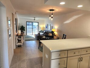 A kitchen with a large island, a dining area with a table and chairs, and a view through a glass door to the outside. - 204 - Completely Renovated 2/2 Partial Views (New Smyrna Beach)