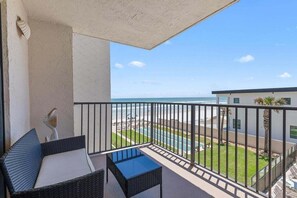 Een balkon met uitzicht op de oceaan, een zwembad en een gebouw met palmbomen.