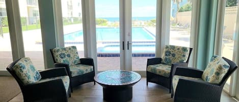 A room with four wicker chairs with floral cushions, a central coffee table, and large glass doors leading to a pool area.