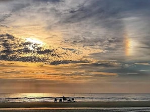 Une scène de plage au coucher du soleil, avec quelques personnes et des cannes à pêche.