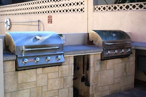 Two stainless steel gas grills with control knobs, a lifebuoy, and a 'No Glass in Pool Area' sign on a patio with a lattice fence. - 310 - Incredible ocean and pool views 1 bedroom (New Smyrna Beach)