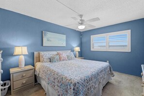 A bedroom with a bed, nightstands, a ceiling fan, a window, and a wall-mounted artwork. - 310 - Incredible ocean and pool views 1 bedroom (New Smyrna Beach)