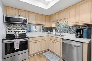 Una cocina moderna con electrodomésticos de acero inoxidable, armarios de madera clara y un tragaluz.