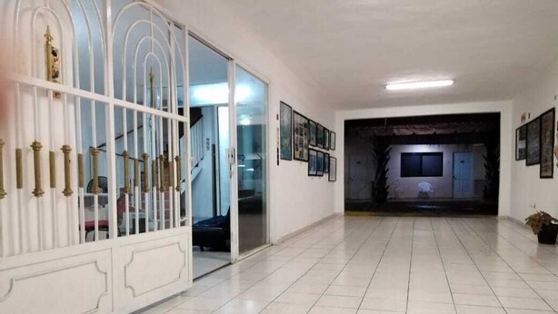 Un pasillo amplio con suelo de baldosas, un portón decorativo blanco y cuadros en las paredes.