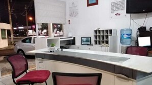 Un área de recepción con mostrador, dos sillas rojas, dispensador de agua y un televisor.