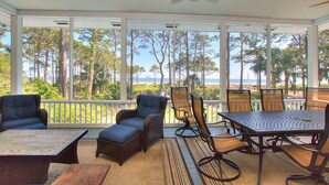 Un espace extérieur abrité, doté d’une table et de chaises, d’un ventilateur de plafond et offrant une vue sur la plage et les palmiers.