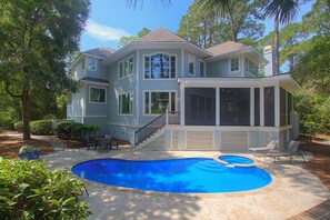 Une maison à deux étages dotée d’un grand jardin à l’arrière, comprenant une piscine, un patio couvert et un escalier menant à l’étage supérieur.