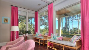 Ein Zimmer mit Korbmöbeln, großen Fenstern und rosa Vorhängen.