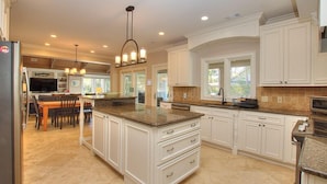 A spacious kitchen with white cabinetry, a large island, and a dining area with a table and chairs. - 26 Surf Scoter - 2nd Row Luxury Home in Sea Pines w/ Private Pool & Spa (Hilton Head Island)