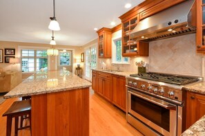 Una cocina con armarios de madera, encimeras de granito, una estufa de acero inoxidable y una isla grande con taburetes de bar.