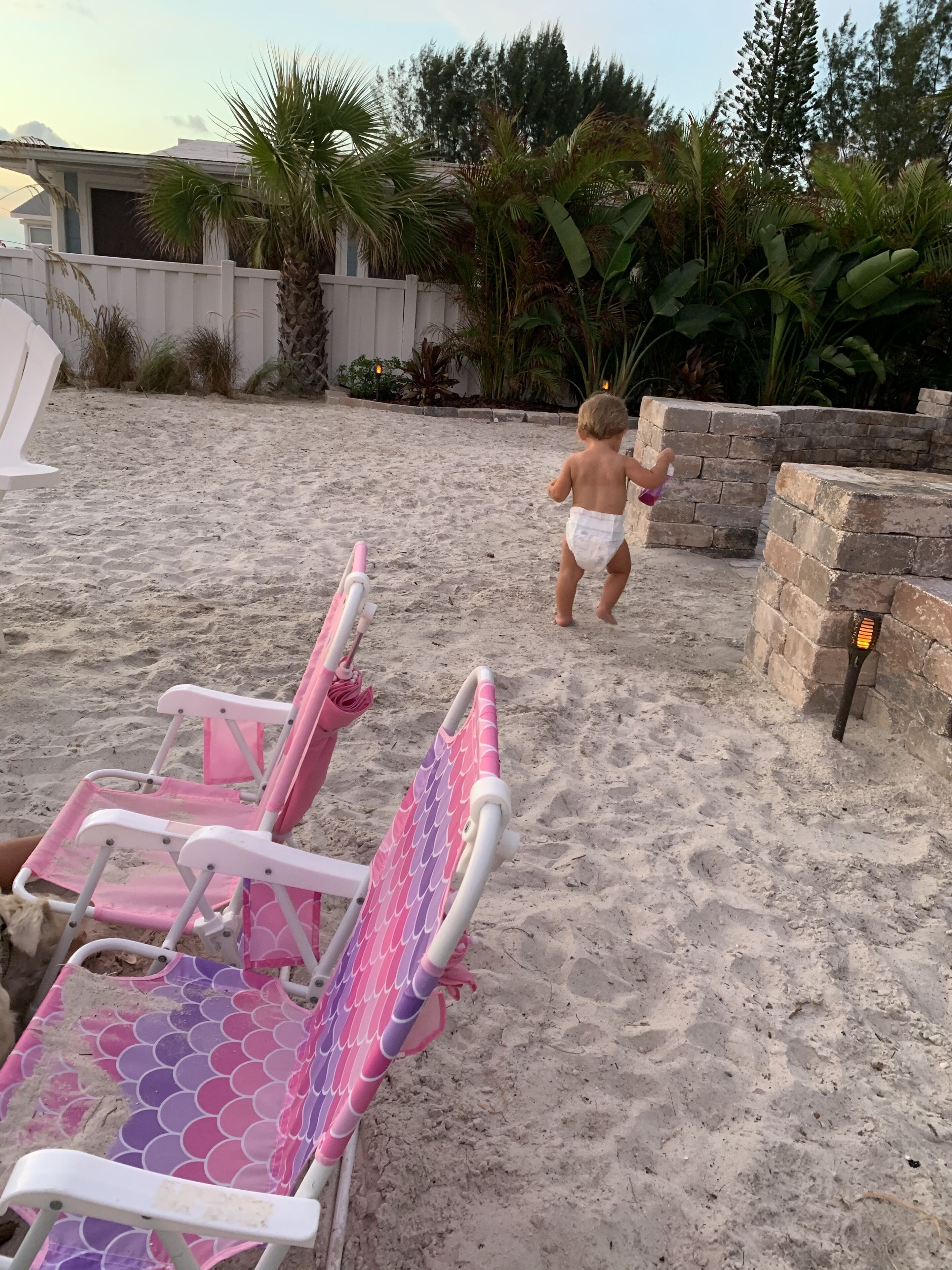 Une plage de sable où un enfant s’éloigne de l’appareil photo et se dirige vers une clôture blanche.